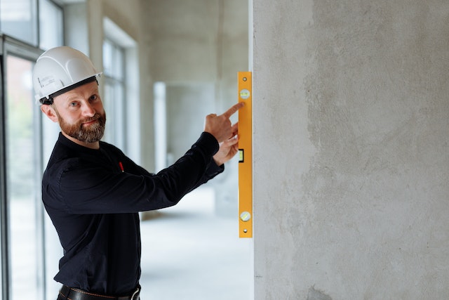 contractor in a white hard hat using an orange level on a wall
